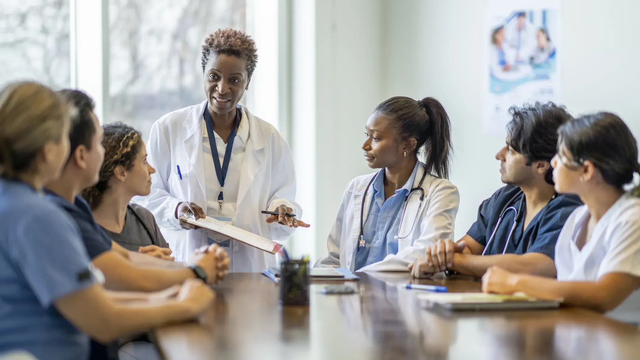 Researchers sitting around a table while one standing at the head of the table speaks