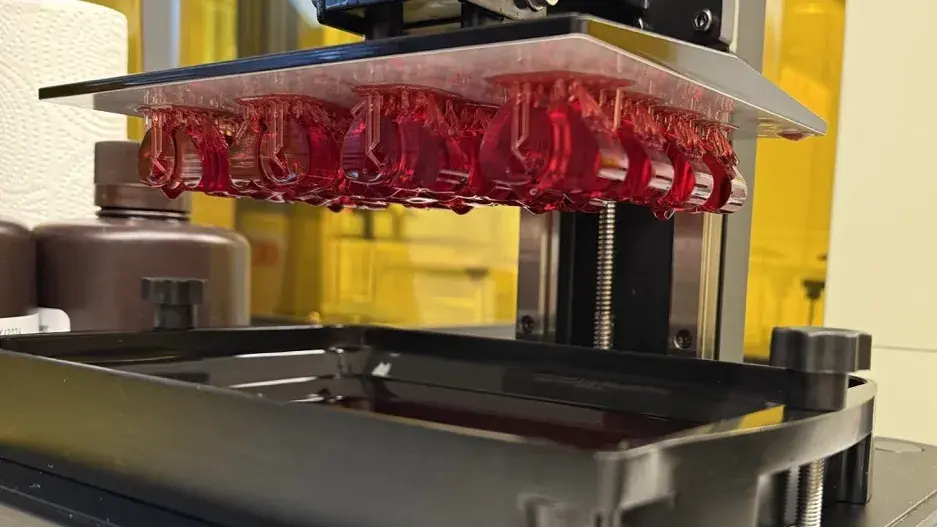 A close up of a 3D resin printer with 3D printed items suspended from the build plate