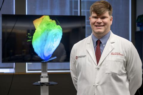 Dr. Blair Suter standing and smiling in front of a anatomical heart on a display.